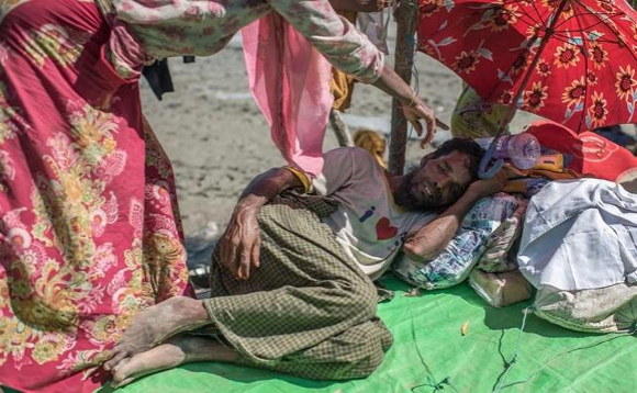 A very sick man is shielded from the sun by his wife at a border crossing in Bangladesh. Refugees have to wait a few days, usually exposed to the elements, before they are allowed to go to the transit centers and refugee camps. Atom Araullo